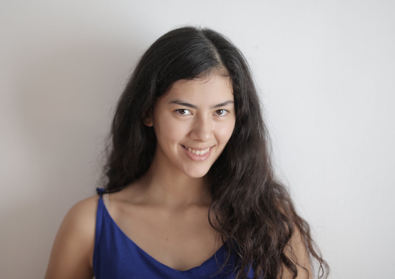 Young long haired brunette without makeup smiling and looking at camera while standing against white background